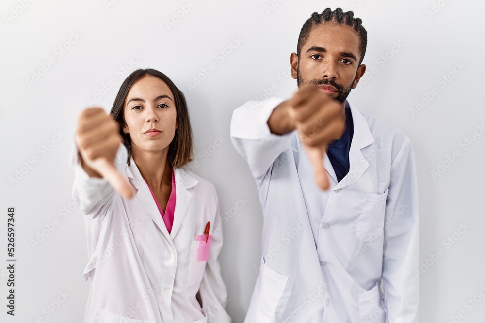 Canvas Prints Young hispanic doctors standing over white background looking unhappy and angry showing rejection and negative with thumbs down gesture. bad expression.