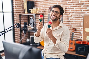 Young hispanic man musician singing song playing maracas at music studio
