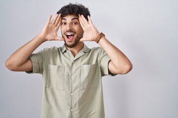 Arab man with beard standing over white background smiling cheerful playing peek a boo with hands showing face. surprised and exited