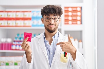 Arab man with beard working at pharmacy drugstore holding condom depressed and worry for distress,...