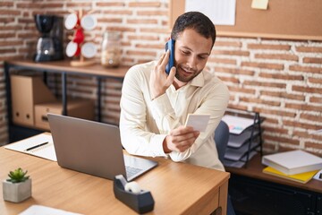 Young man business worker talking on smartphone reading reminder paper at office