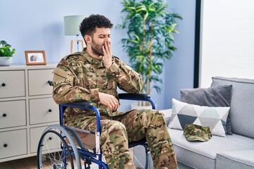 Arab man wearing camouflage army uniform sitting on wheelchair bored yawning tired covering mouth...