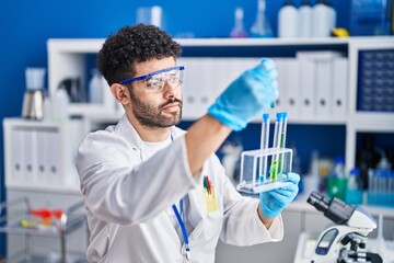 Young arab man wearing scientist uniform holding test tubes at laboratory