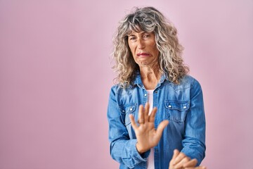 Middle age woman standing over pink background disgusted expression, displeased and fearful doing...