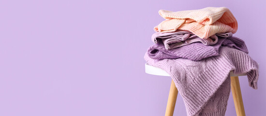 Stack of warm sweaters on table against lilac background with space for text