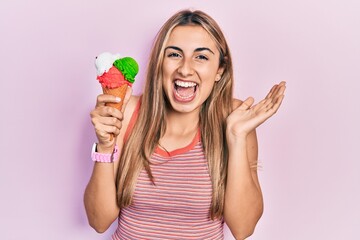 Beautiful hispanic woman holding ice cream celebrating achievement with happy smile and winner expression with raised hand