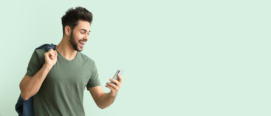 Happy young man with mobile phone on light color background with space for text