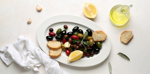 Plate of different olives, bread, oil and lemon on light background