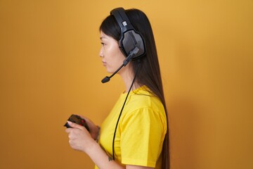 Chinese young woman playing video game holding controller looking to side, relax profile pose with natural face and confident smile. © Krakenimages.com