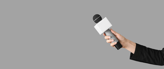 Journalist's hand holding microphone on grey background with space for text