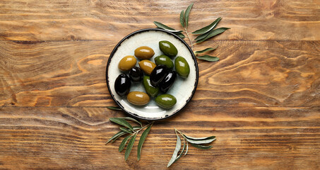 Plate with delicious olives on wooden background