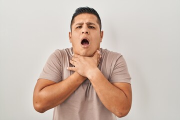 Hispanic young man standing over white background shouting and suffocate because painful strangle. health problem. asphyxiate and suicide concept.