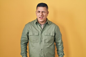 Hispanic young man standing over yellow background winking looking at the camera with sexy...