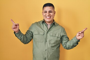 Hispanic young man standing over yellow background smiling confident pointing with fingers to different directions. copy space for advertisement