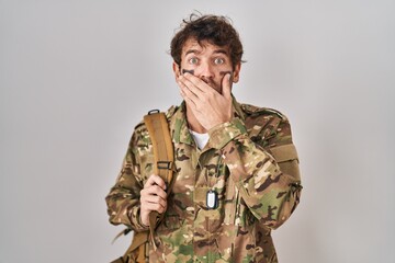 Hispanic young man wearing camouflage army uniform shocked covering mouth with hands for mistake. secret concept.