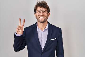 Hispanic business man wearing glasses showing and pointing up with fingers number two while smiling confident and happy.