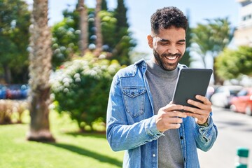 Young hispanic man smiling confident using touchpad at park - obrazy, fototapety, plakaty