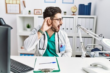 Young man with beard wearing doctor uniform and stethoscope at the clinic smiling with hand over...