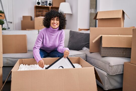 Young middle east woman smiling confident unpacking cardboard box at new home