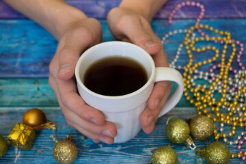 Christmas relax, New year eve. Human hands hold white tea mug. Golden holiday decorations m blue...