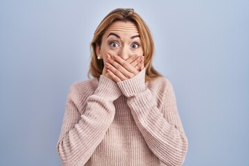 Hispanic woman standing over blue background shocked covering mouth with hands for mistake. secret concept.
