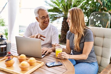 Middle age hispanic couple having breakfast using laptop at the terrace.