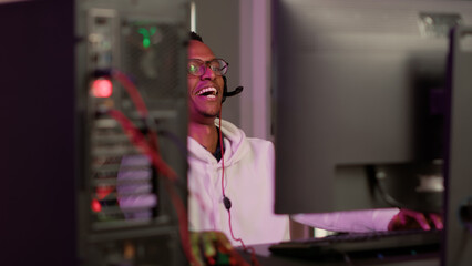 Selective focus on african american gamer using gaming pc professional setup while having fun playing online games at home. Man enjoying relaxing free time streaming multiplayer competition.