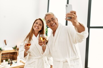 Middle age hispanic couple drinking champagne make selfie by the smartphone at wellness center.