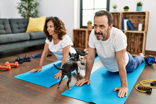 Middle Age Hispanic Couple Smiling Happy Stretching On The Floor At Home.