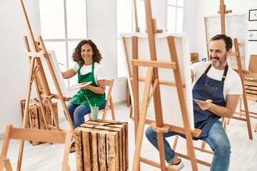 Two middle age student smiling happy painting at art studio.