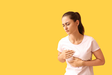 Young woman suffering from breast pain on yellow background