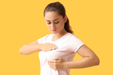 Young woman suffering from breast pain on yellow background
