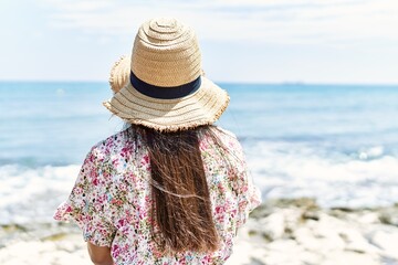 Young latin girl on back view wearing summer hat sitting on the bench at the beach.