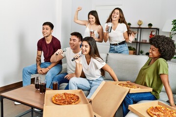 Group of young friends having party eating italian pizza and singing song at home.