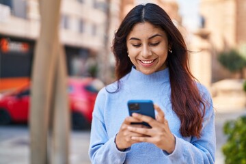 Fototapeta premium Young hispanic woman smiling confident using smartphone at street