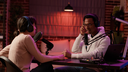 African american internet show host interviewing famous influencer while adjusting headphones in...