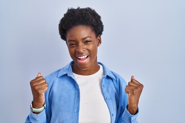 African american woman standing over blue background celebrating surprised and amazed for success with arms raised and eyes closed. winner concept.