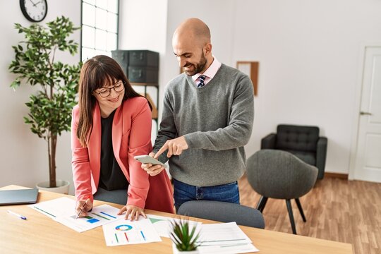 Two hispanic business workers smiling happy working using smartphone at the office.
