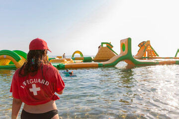 Lifeguard on rescue duty, standing on shore with whistle and looking to the Aquapark. Safety...