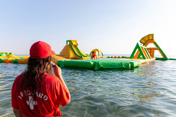Lifeguard on rescue duty, standing on shore with whistle and looking to the Aquapark. Safety control on vacation. Babysitting on the water