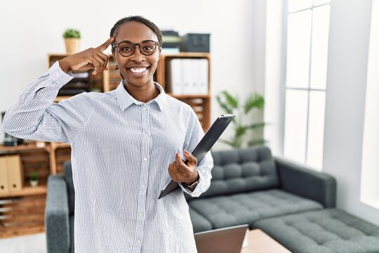 African woman working at psychology clinic smiling pointing to head with one finger, great idea or thought, good memory