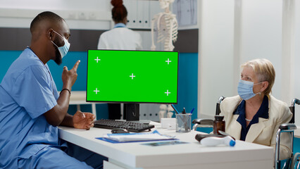 Man and patient with impairment using computer with greenscreen, checkup during pandemic. Looking at blank mockup copyspace with isolated chromakey template, woman with disability in wheelchair.