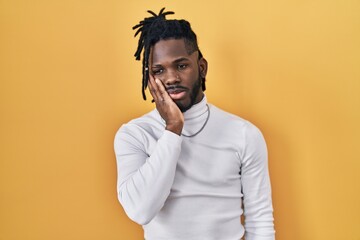 Obraz premium African man with dreadlocks wearing turtleneck sweater over yellow background thinking looking tired and bored with depression problems with crossed arms.
