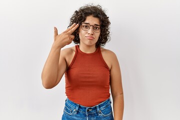 Young hispanic woman wearing glasses standing over isolated background shooting and killing oneself pointing hand and fingers to head like gun, suicide gesture.