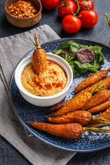 Plate with tasty baked carrots and bowl of sauce on table, closeup