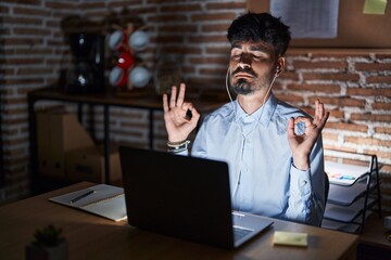 Young hispanic man with beard working at the office at night relax and smiling with eyes closed doing meditation gesture with fingers. yoga concept.