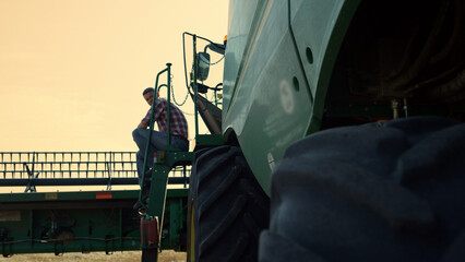 Farmer resting combine field at sunset. Tired worker inspecting stubble farmland