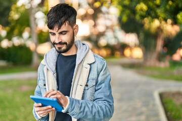 Fototapeta premium Young hispanic man smiling confident using touchpad at park