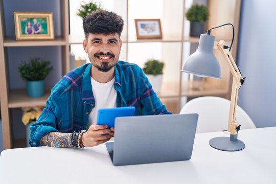 Young hispanic man using laptop and touchpad sitting on table at home