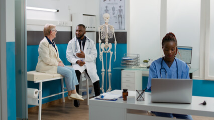 African american medic consulting senior patient in cabinet, talking about healthcare treatment and medicine to cure disease. Woman and doctor doing checkup visit examination at clinic.